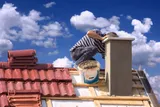 Chimney sweep in protective gear working on a rooftop chimney