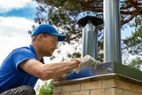 Chimney technician on a rooftop next to a metal chimney cap