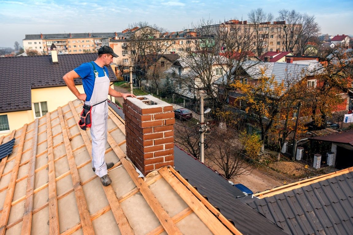 Chimney technician standing on a roof beside a brick chimney, inspecting it