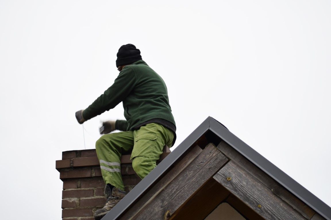 Chimney sweep on a rooftop with brushes and rods, back turned